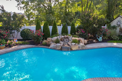 Multnomah G - West Deptford, NJ - A swimming pool surrounded by lush greenery and flowers, with a waterfall feature