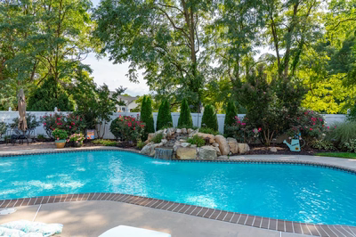 Multnomah H - West Deptford, NJ - A swimming pool surrounded by lush greenery and flowers, with a waterfall feature