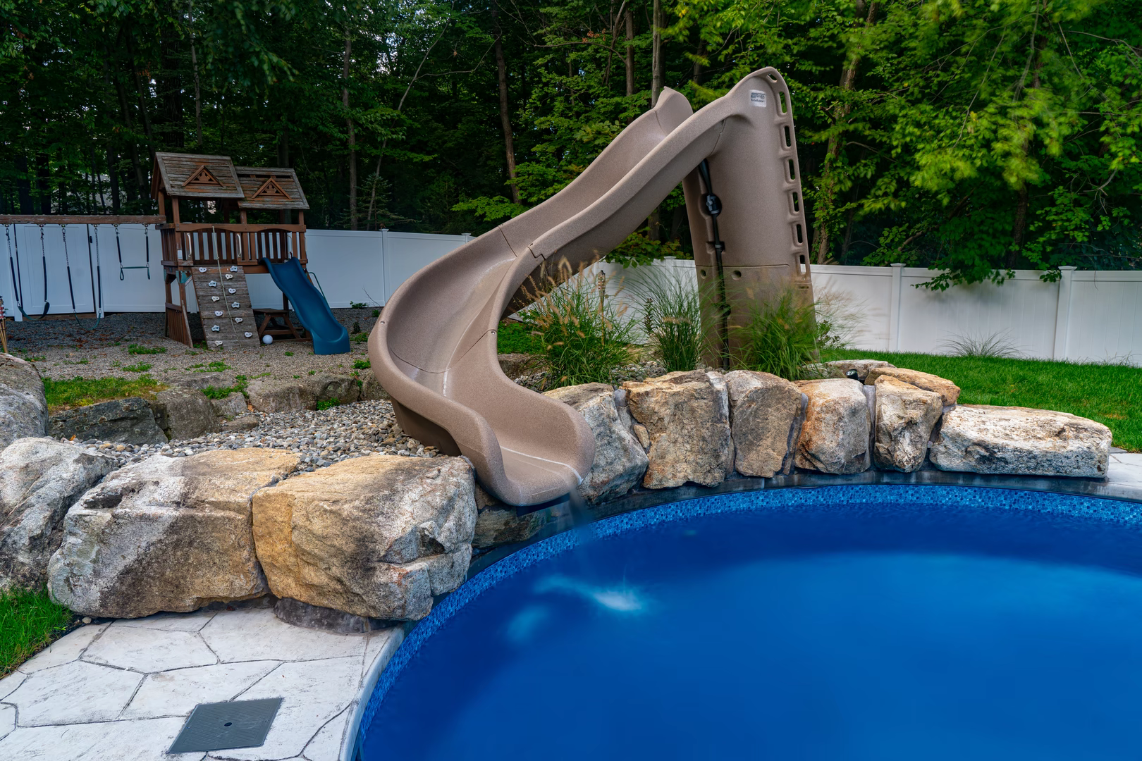 Natural stone boulder waterfall cascading into a swimming pool surrounded by lush greenery