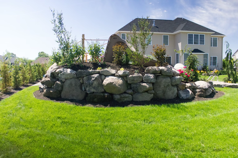Natural stone boulder waterfall cascading into a pool surrounded by lush garden greenery