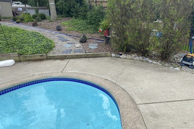 Nachi C - Medford Lakes, NJ - A concrete pool deck with a blue tiled border and a small garden area in the background