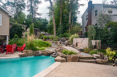 Nachi I - Medford Lakes, NJ - A backyard with a swimming pool surrounded by lush greenery and rocks