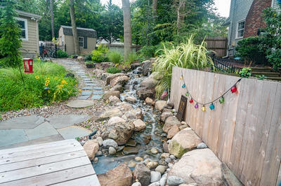 Nachi O - Medford Lakes, NJ - A small stream running through a lush green garden next to a wooden fence