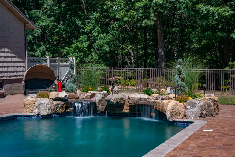 Natural stone boulder waterfalls cascading into a swimming pool surrounded by lush greenery