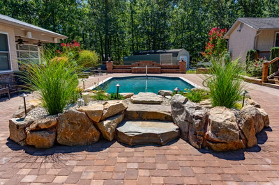 Naena F - Newfield, NJ - A backyard with a swimming pool surrounded by lush greenery and rocks