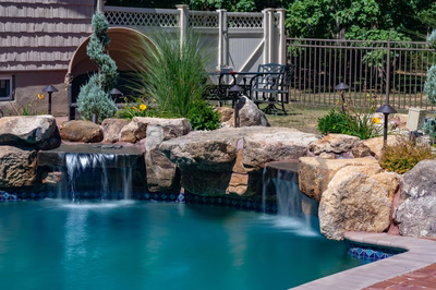 Naena H - Newfield, NJ - A swimming pool with a waterfall feature surrounded by rocks and plants