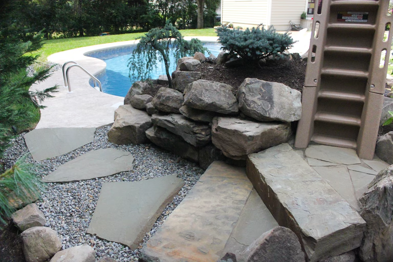 Natural stone boulder waterfall cascading into a pool surrounded by lush evergreen plants