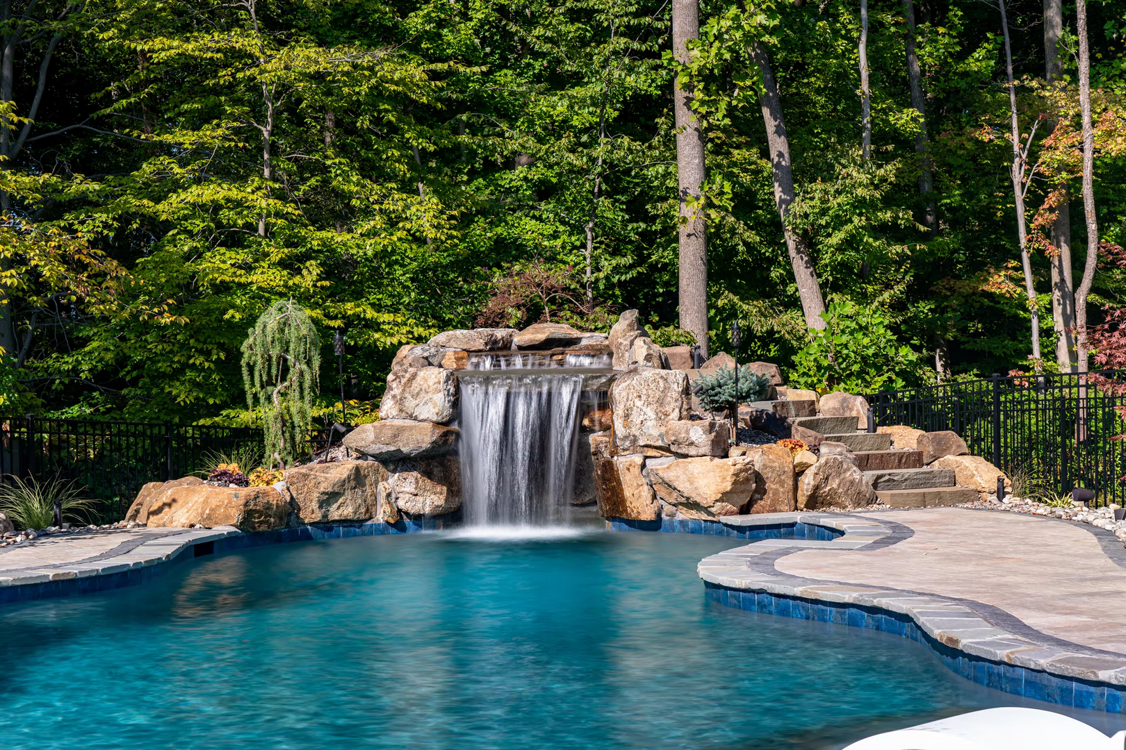 Natural stone boulder waterfall cascading into a freeform pool with lush forest surroundings