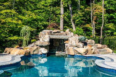 Niagara B - Bel Air, MD - A swimming pool surrounded by lush green trees and a stone waterfall.