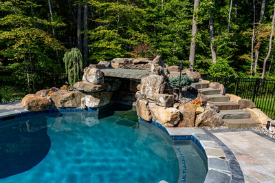 Niagara D - Bel Air, MD - A swimming pool with a rock waterfall and steps leading up to it surrounded by lush greenery