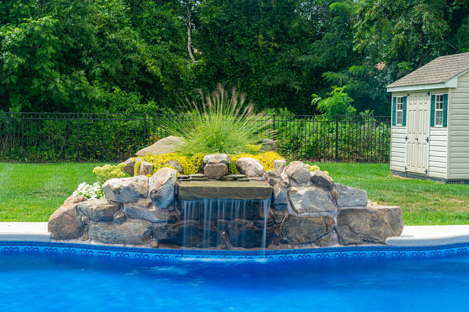 Natural stone boulder waterfall cascading into a pool with surrounding ornamental plants