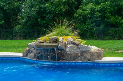 Okere E - Freehold, NJ - A rock waterfall in the middle of a swimming pool surrounded by lush green grass and trees
