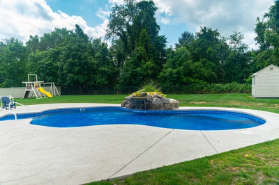 Okere F - Freehold, NJ - A backyard with a swimming pool and a play area surrounded by trees