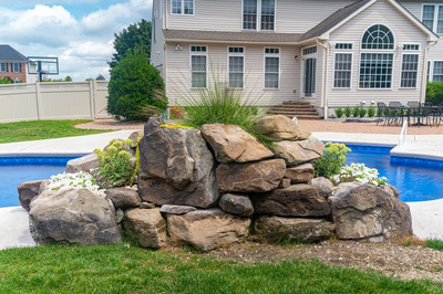 Okere H - Freehold, NJ - A large rock wall next to a swimming pool in a backyard.