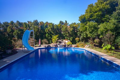 Oneonta D - Hamilton Square, NJ - A blue swimming pool surrounded by lush greenery and a water feature
