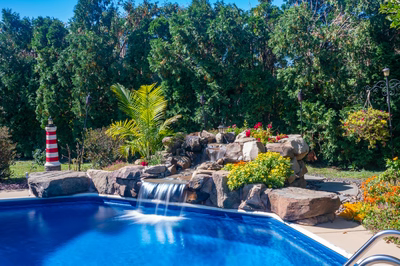 Oneonta E - Hamilton Square, NJ - A swimming pool with a waterfall surrounded by lush greenery and colorful flowers