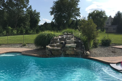 Osawa A - Millstone, NJ - A swimming pool with a waterfall in the middle of it surrounded by lush greenery and trees