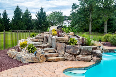 Osawa D - Millstone, NJ - A backyard with a swimming pool and a rock waterfall feature