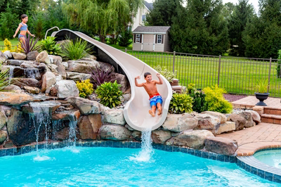 Osawa E - Millstone, NJ - A boy sliding down a water slide into a swimming pool surrounded by rocks and plants
