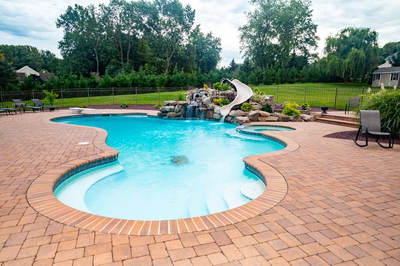 Osawa F - Millstone, NJ - A swimming pool with a waterfall in the middle surrounded by lush greenery