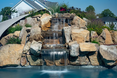 Otaki B - Ivyland, PA - A large rock waterfall in a backyard setting with a house in the background