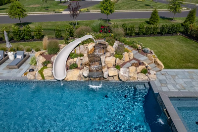 Otaki C - Ivyland, PA - A swimming pool with a waterfall and a water slide surrounded by lush greenery