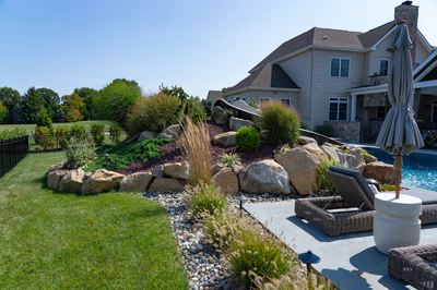 Otaki I - Ivyland, PA - A backyard with a large house and a pool surrounded by lush green grass and rocks