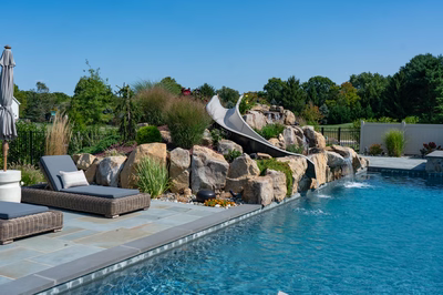 Otaki J - Ivyland, PA - A swimming pool with a water feature and rock wall, surrounded by lush greenery