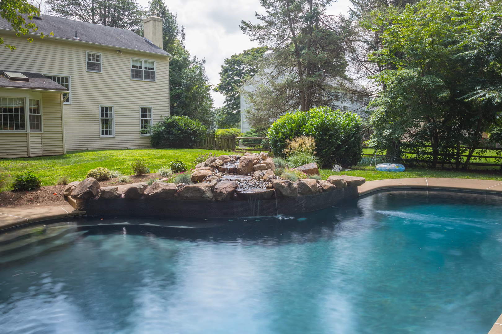 Natural stone boulder waterfall cascading into a swimming pool beside lush garden plants