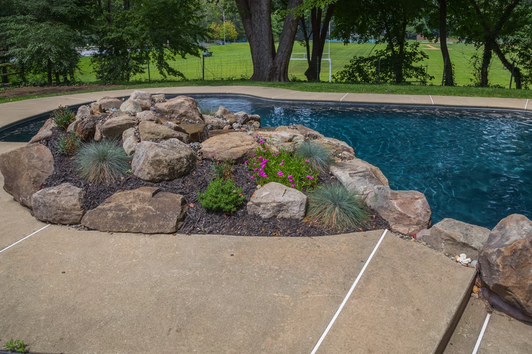 Natural stone boulder waterfall cascading into a pool with ornamental grasses and flowers