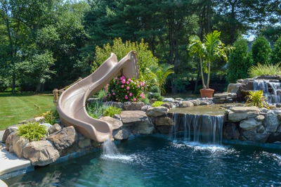 Paradise B - Moorestown, NJ - A backyard pool with a slide and waterfall surrounded by lush greenery