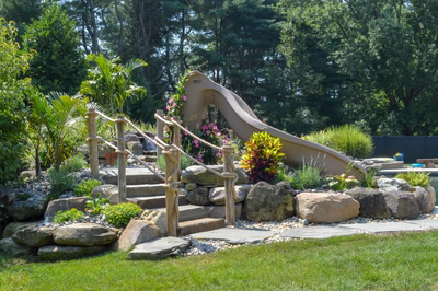Paradise C - Moorestown, NJ - A natural stone play area with a wooden play structure and a water feature surrounded by lush greenery