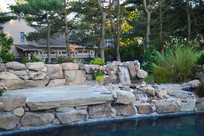 Paradise G - Moorestown, NJ - A swimming pool with a water feature and a slide surrounded by lush greenery