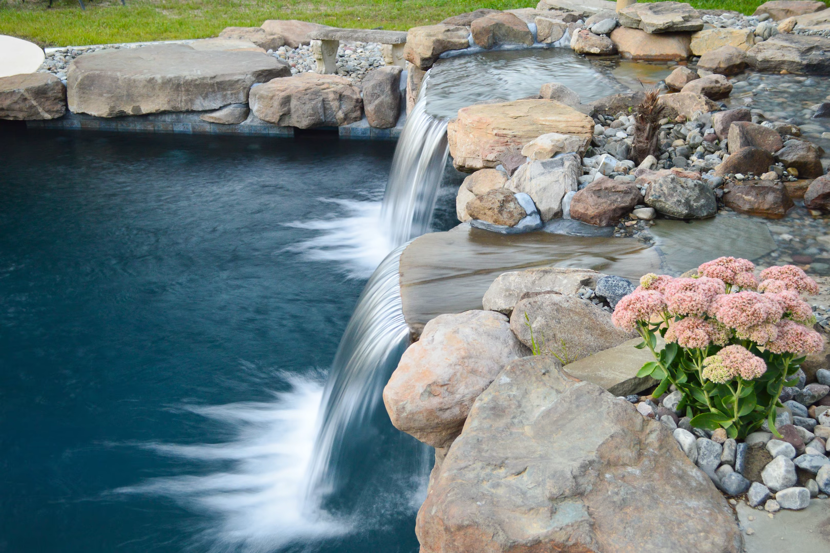 Paradise J - Moorestown, NJ - A backyard pool with a waterfall and a slide surrounded by lush greenery