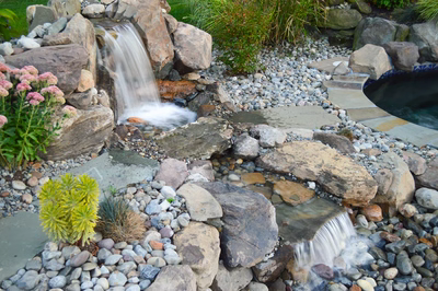 Paradise L - Moorestown, NJ - A small waterfall cascades over rocks and pebbles in a garden setting