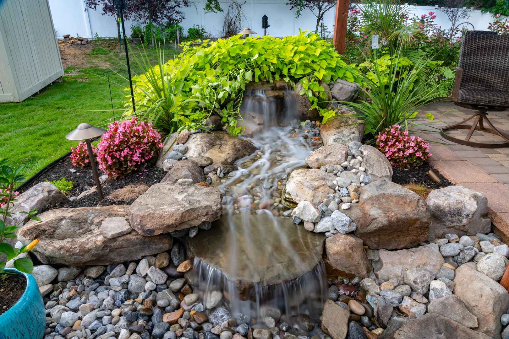 Natural stone boulder waterfall cascading elegantly through lush greenery and vibrant garden plants