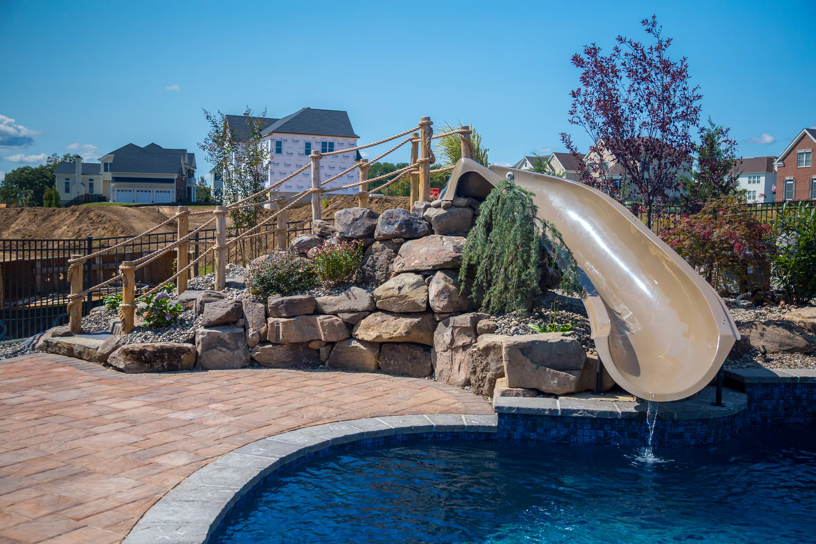 Natural stone boulder waterfall cascading into a pool surrounded by lush garden plants