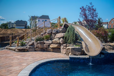 Pearl A - Lincroft, NJ - A backyard with a water slide and a pool surrounded by landscaping