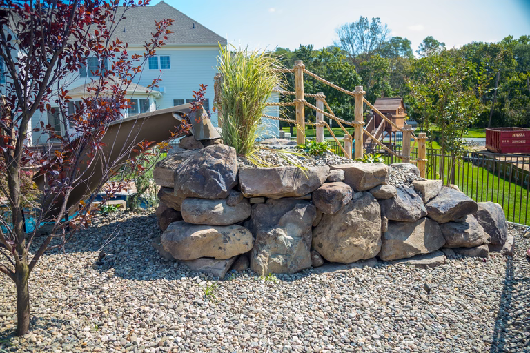 Natural stone boulder waterfall cascading into a pool surrounded by gravel and plants