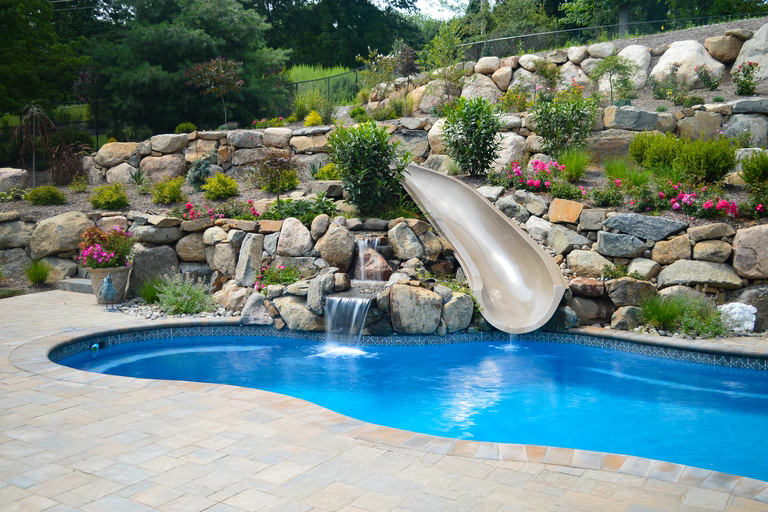 Natural stone boulder waterfall cascading into a freeform pool with lush garden landscaping