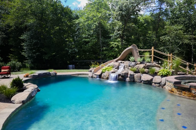 Pongour D - Mt. Laurel, NJ - A swimming pool with a water feature and a slide surrounded by lush greenery
