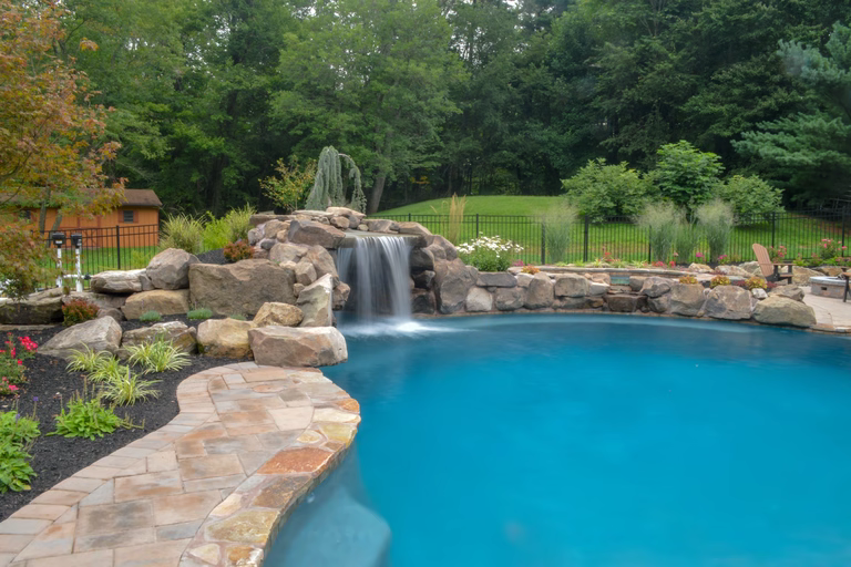 Natural stone boulder waterfall cascading into a freeform pool with lush garden landscaping