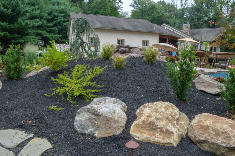 Natural stone boulder waterfall cascading into a backyard pool surrounded by lush plants