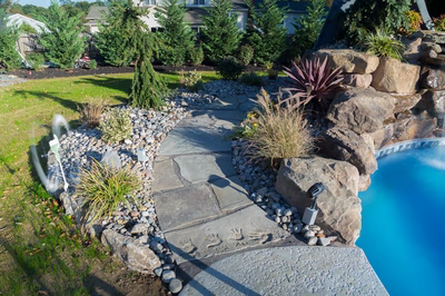 Rainbow B - Middletown, NJ - A stone path leading to a swimming pool surrounded by lush greenery and rocks