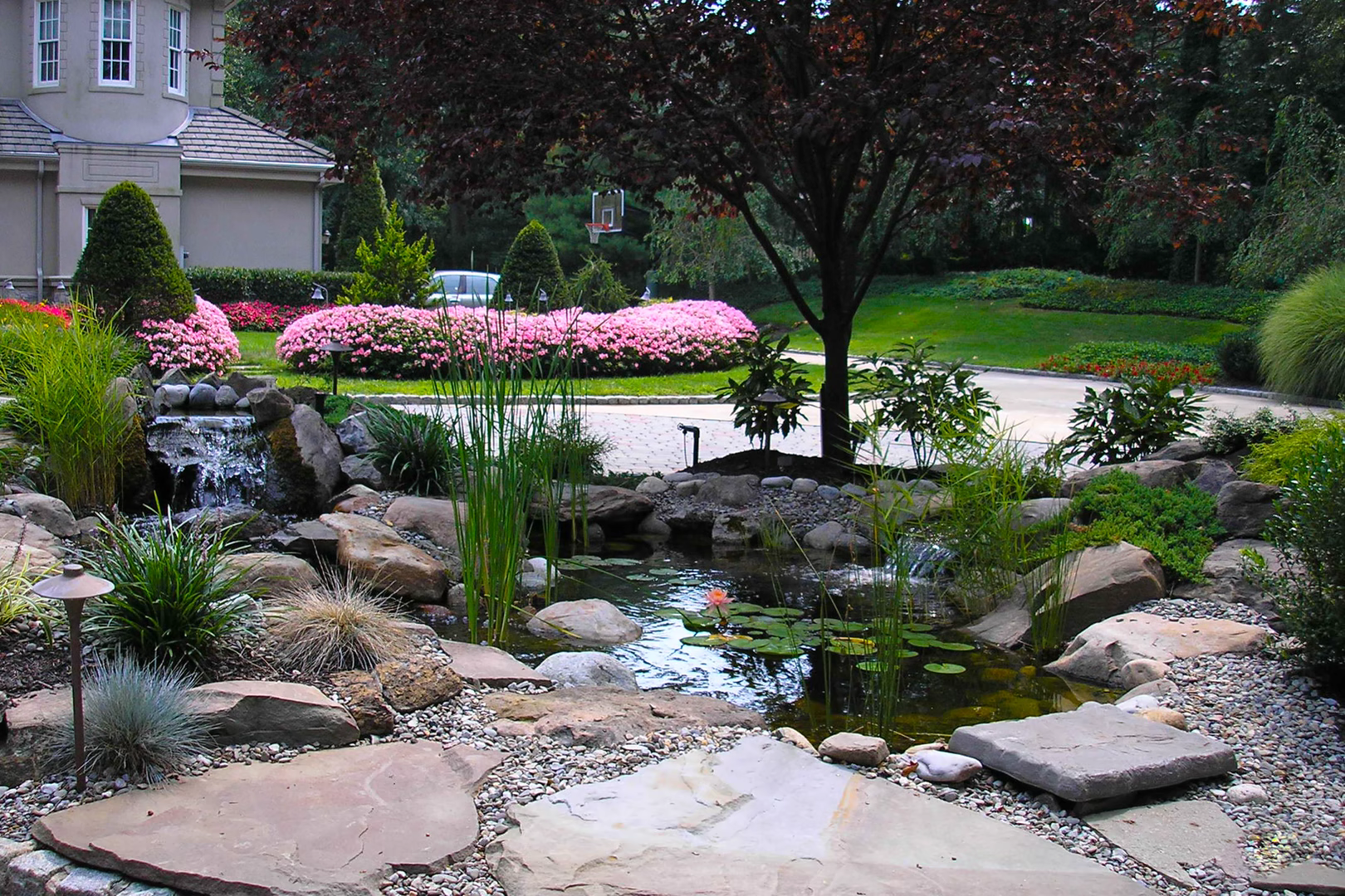 Natural stone boulder waterfalls cascading into a garden pond surrounded by lush plants