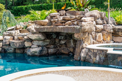 Richetli D - Monroe, NJ - A swimming pool with a waterfall feature in the middle surrounded by lush greenery