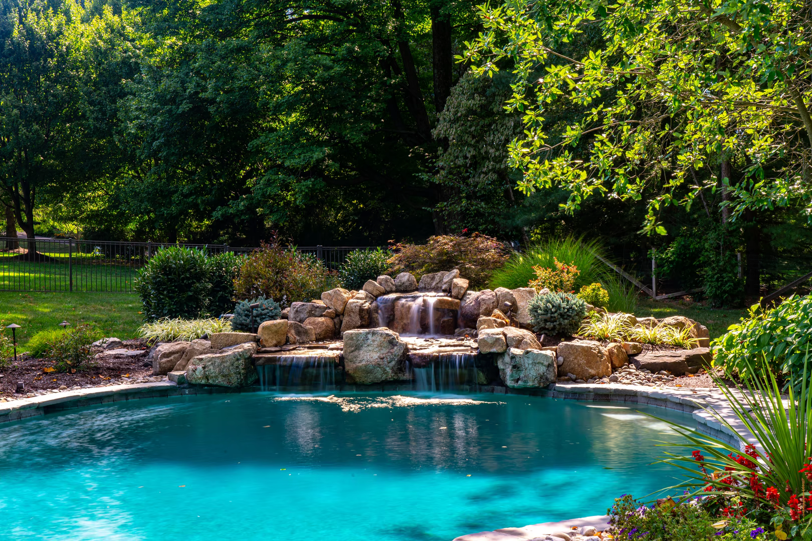 Natural stone boulder waterfall cascading into a swimming pool surrounded by lush greenery