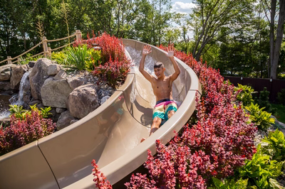 Roesch D - Englishtown, NJ - A young boy sliding down a water slide at a water park surrounded by lush greenery