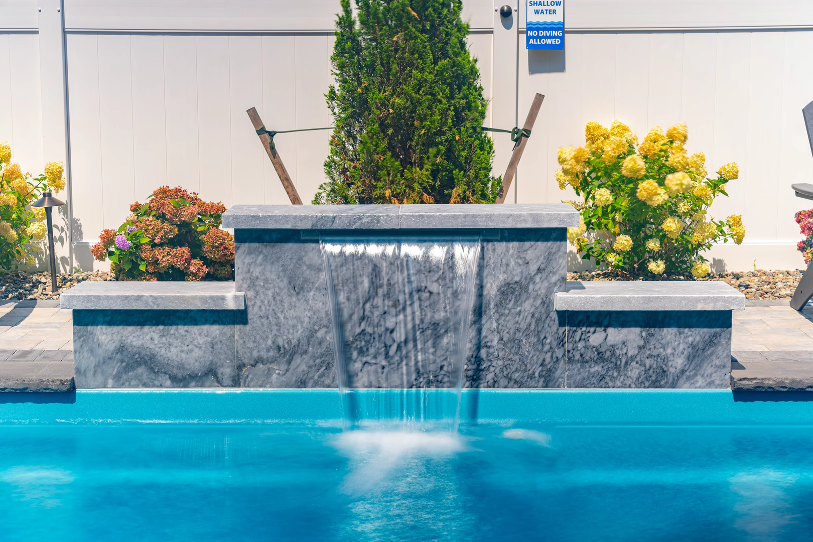 Stone waterfall with sheet flow cascading into a pool beside colorful plants