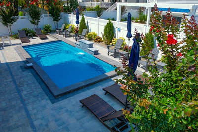 Rome H - Long Beach Island, NJ - A rectangular swimming pool surrounded by lush greenery and flowers, with lounge chairs and umbrellas